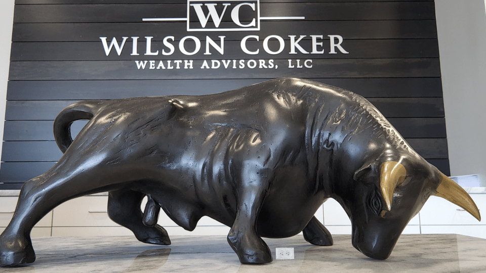 Bronze bull statue displayed on a countertop in front of a sign reading 'Wilson Coker Wealth Advisors, LLC.